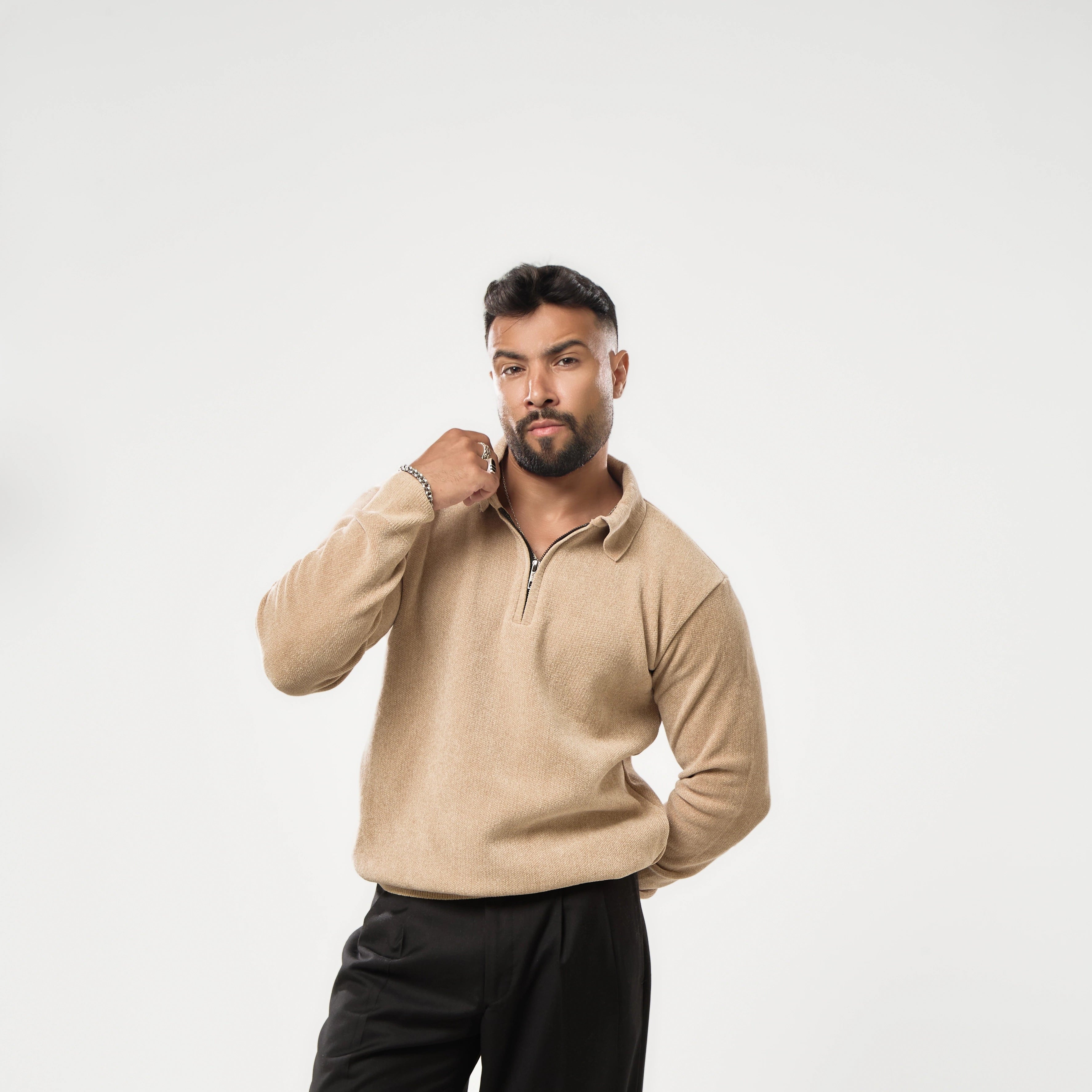 Man wearing a beige sweater and black pants on a white background